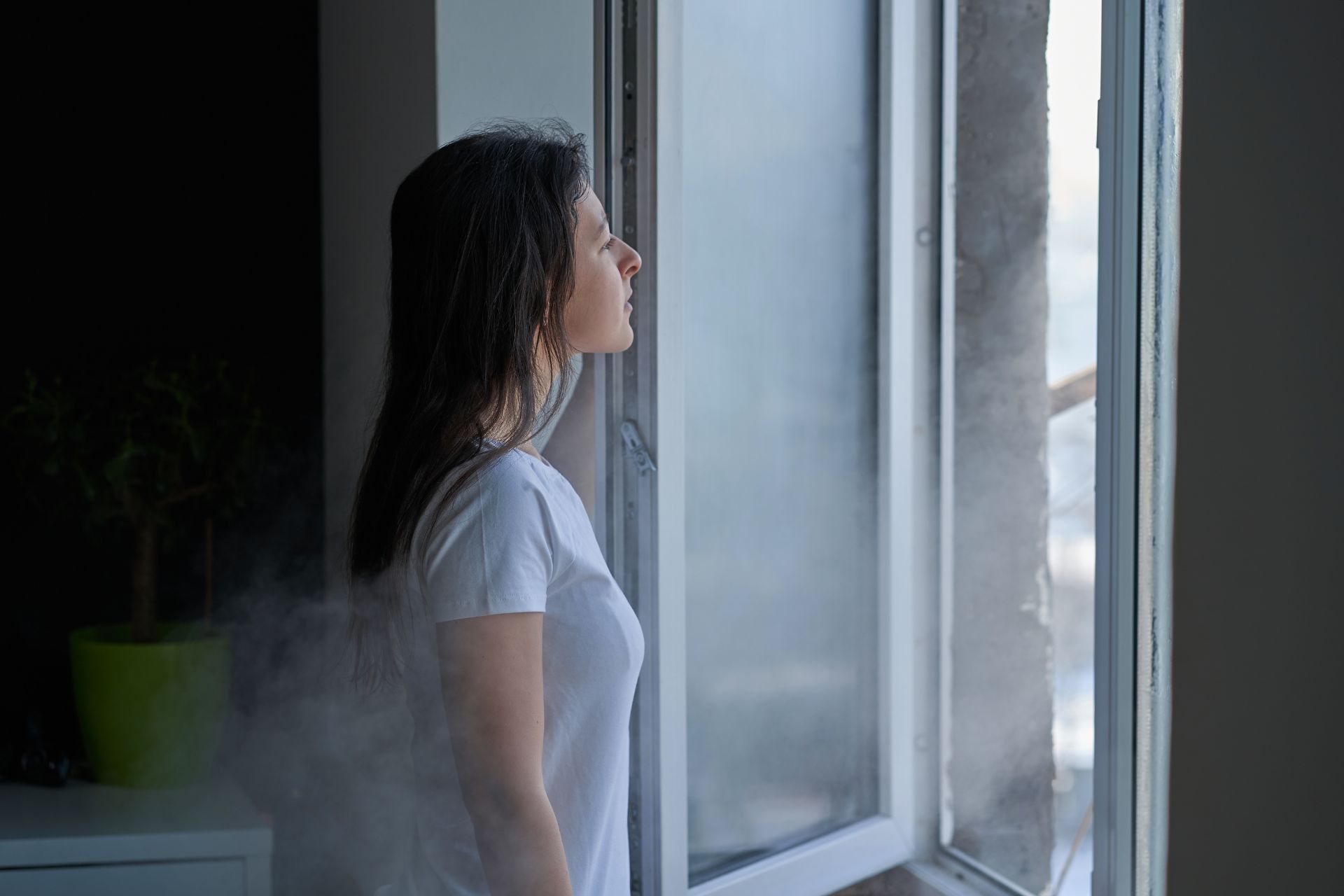 A woman in a white T-shirt opens the window to improve winter indoor air quality