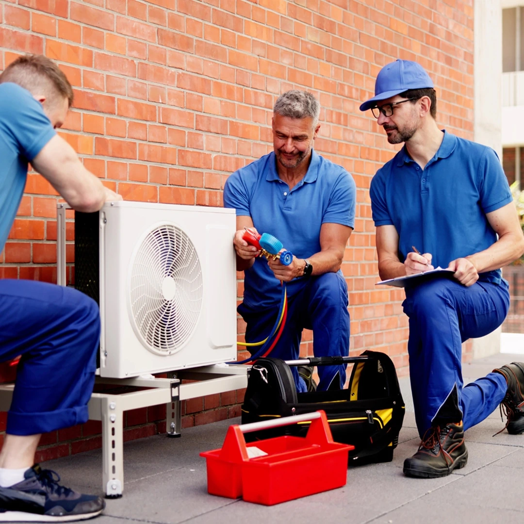 Three technicians inspecting an outdoor HVAC unit