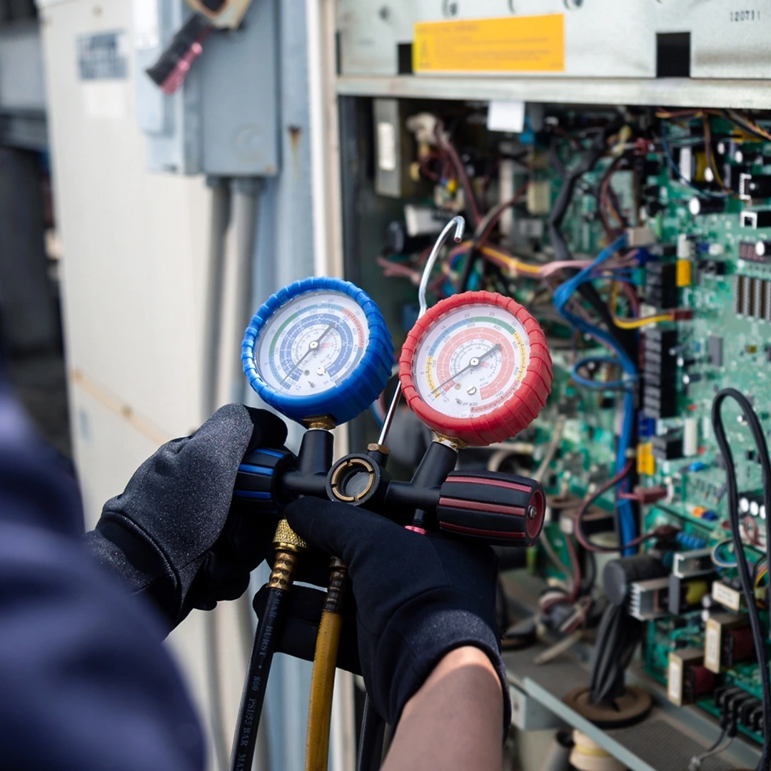 HVAC service technician using gauges to check refrigerant from an AC unit