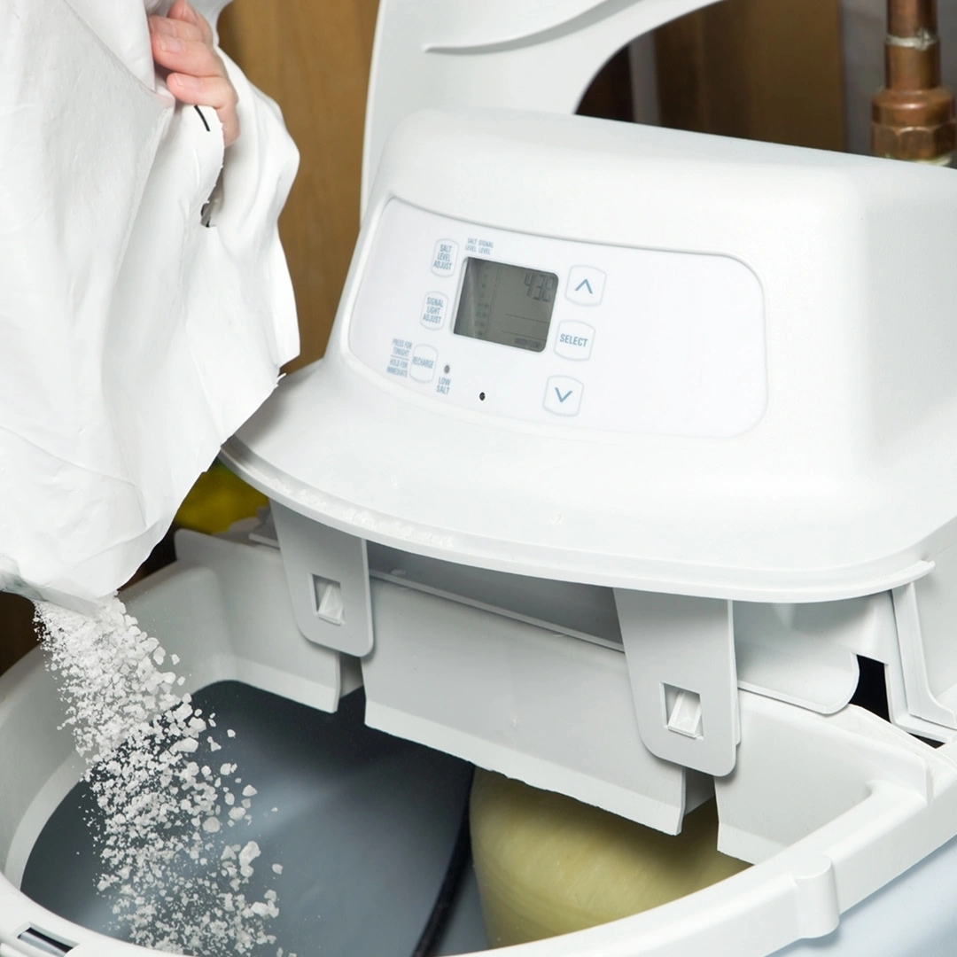 A person filling a water softener brine tank with salt