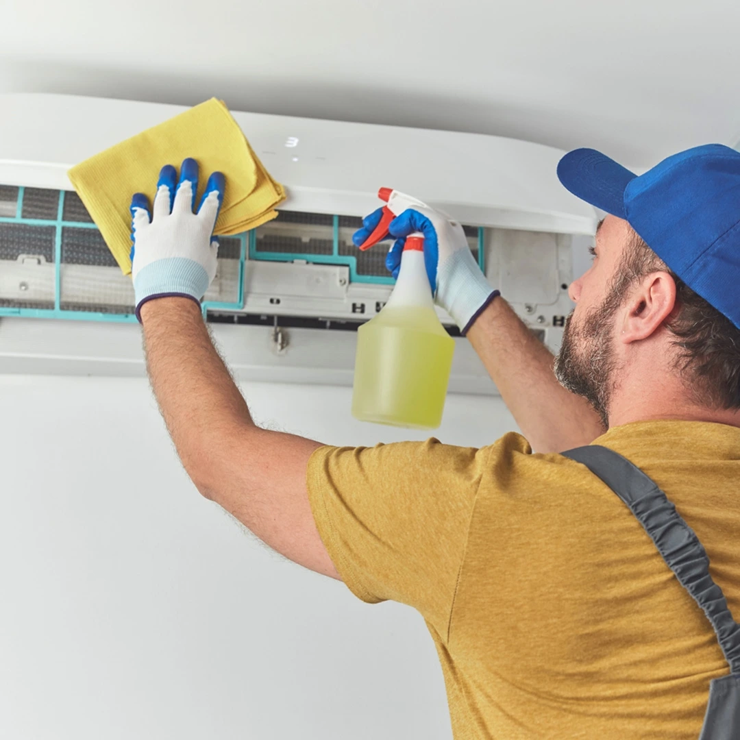 HVAC technician cleaning an AC unit with a cleaning spray and cloth