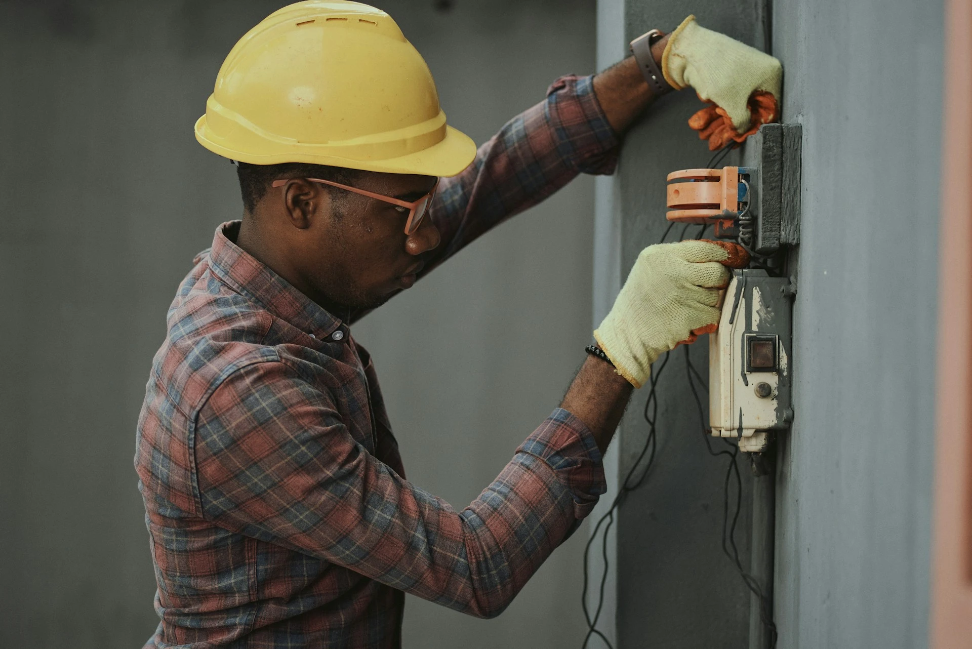 A male technician in a yellow hard hat working on an electrical panel 